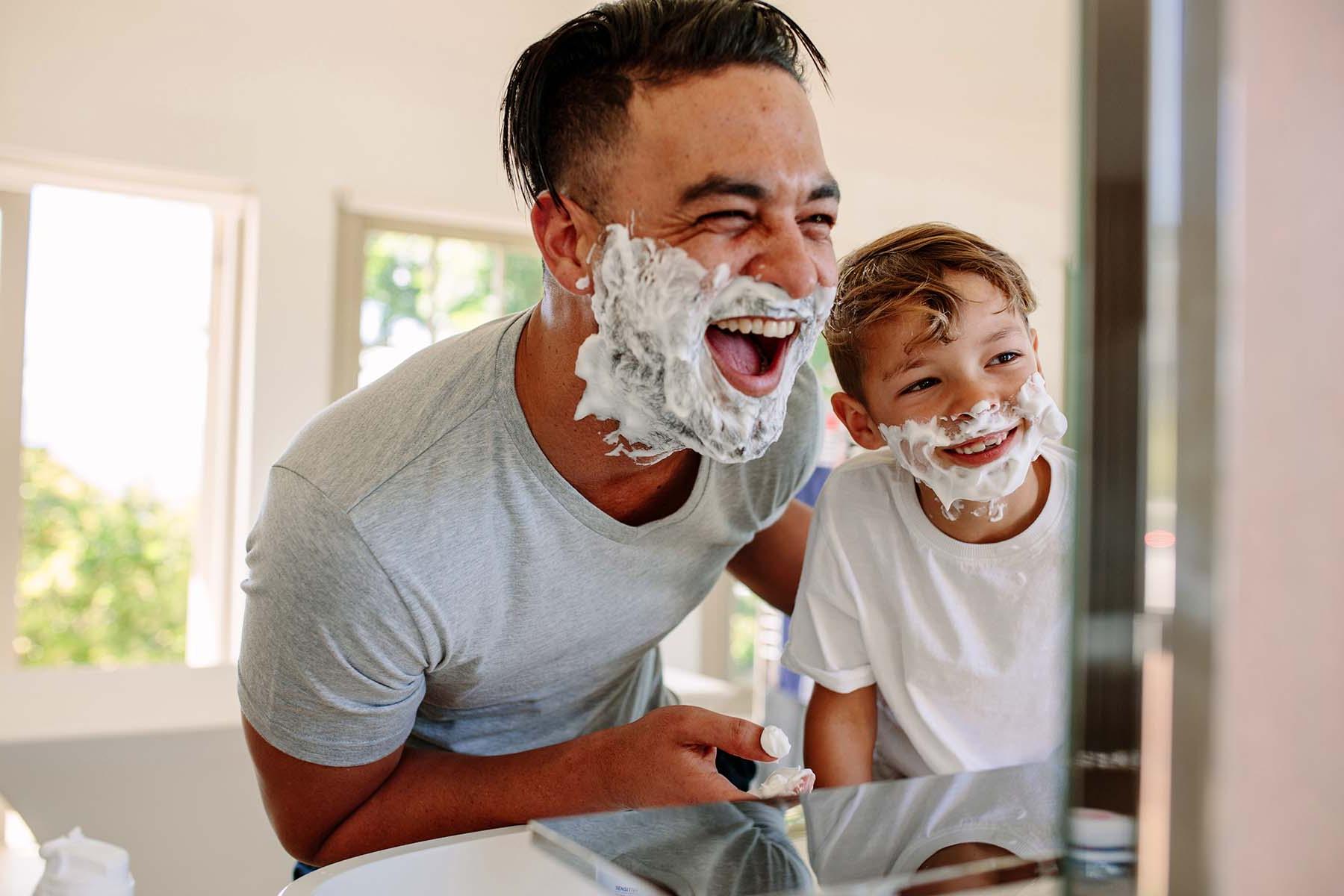 脸上涂着剃须膏的男人和男孩在浴室里大笑.