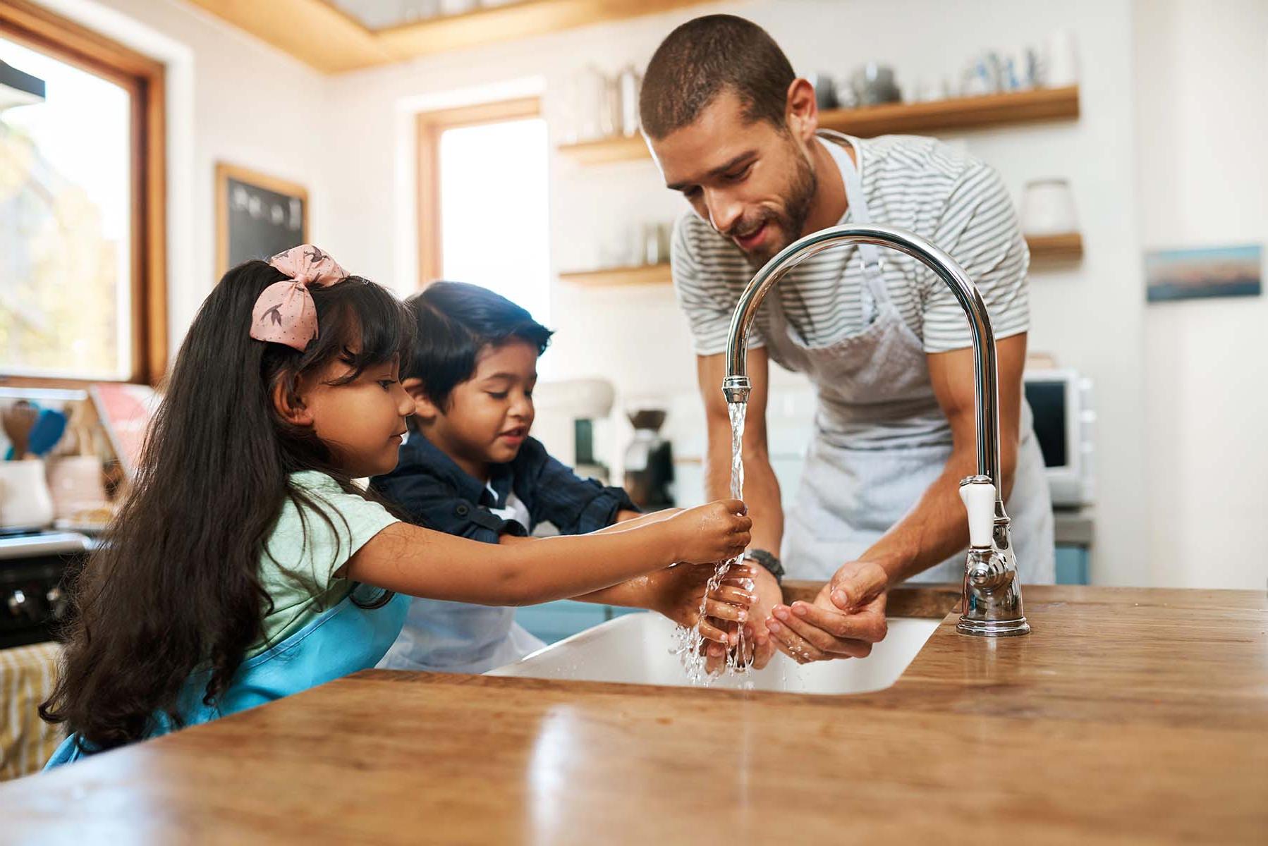一个男人和两个孩子在厨房的水池边洗手